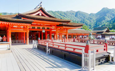 Itsukushima Shrine with red wooden structures and mountainous backdrop in Japan.