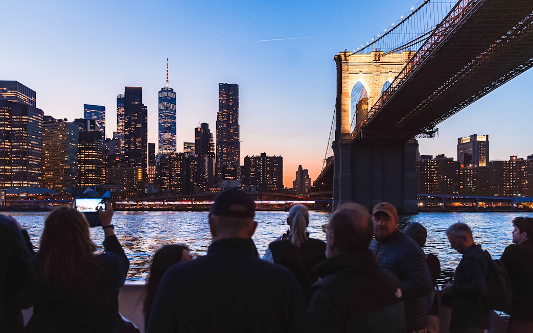 Brooklyn Bridge illuminated at night with New York City skyline in the background.