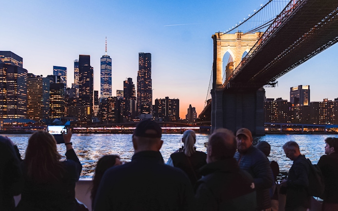 Brooklyn Bridge illuminated at night with New York City skyline in the background.