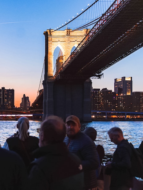 Brooklyn Bridge illuminated at night with New York City skyline in the background.