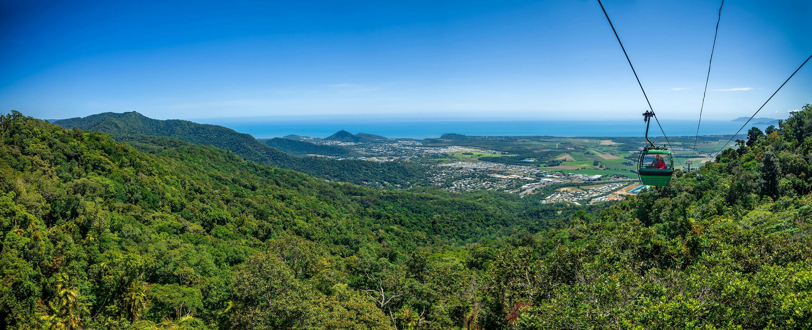 Skyrail gondola over lush rainforest with ocean view, Kuranda, Australia.