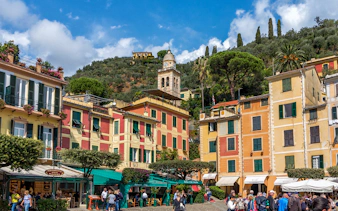 Colorful buildings and a clock tower in Portofino, Italy, with tourists exploring the area.