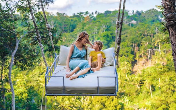 Family enjoying swing bed at Alas Harum, Bali with lush greenery in the background.