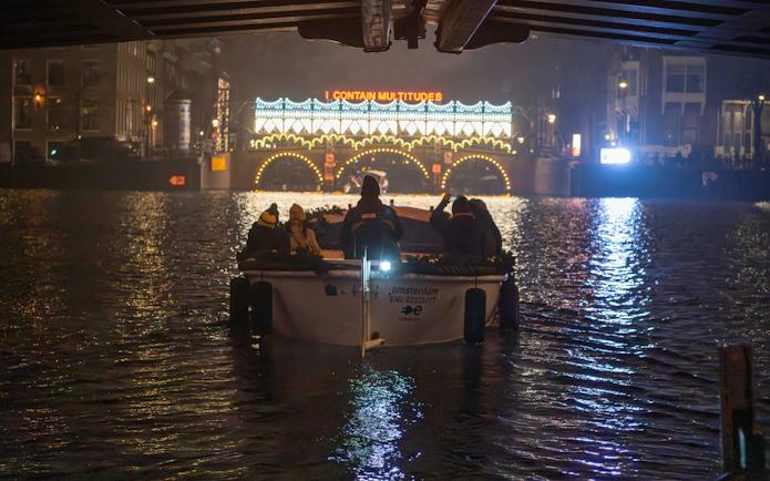 Boat tour under illuminated bridge at Amsterdam Light Festival.