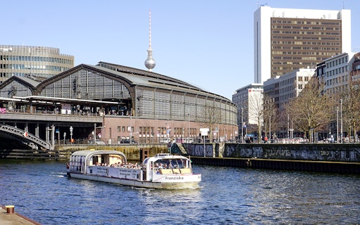 River cruise boat with tour guide passing Berlin's Friedrichstraße station.