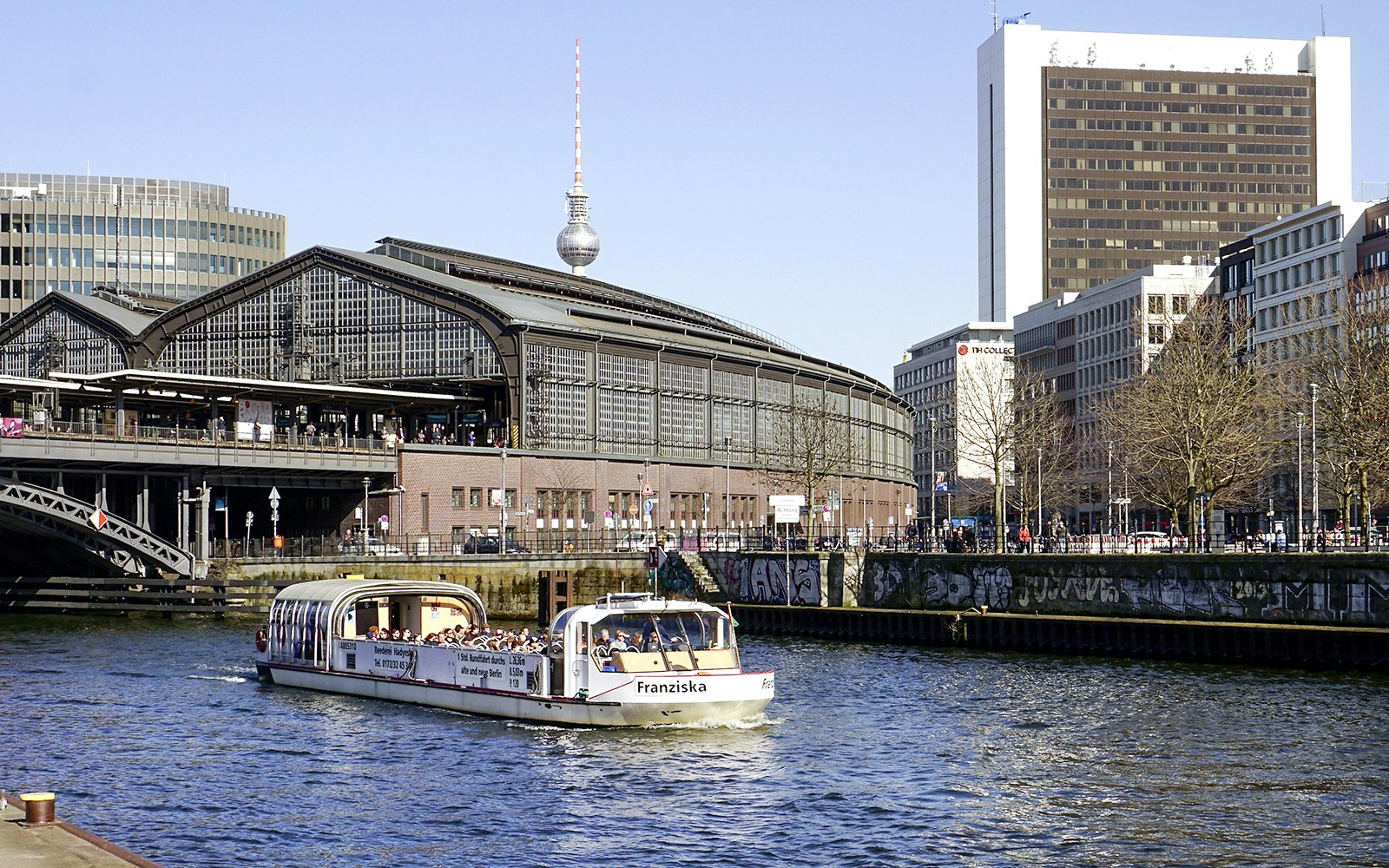 River cruise boat with tour guide passing Berlin's Friedrichstraße station.