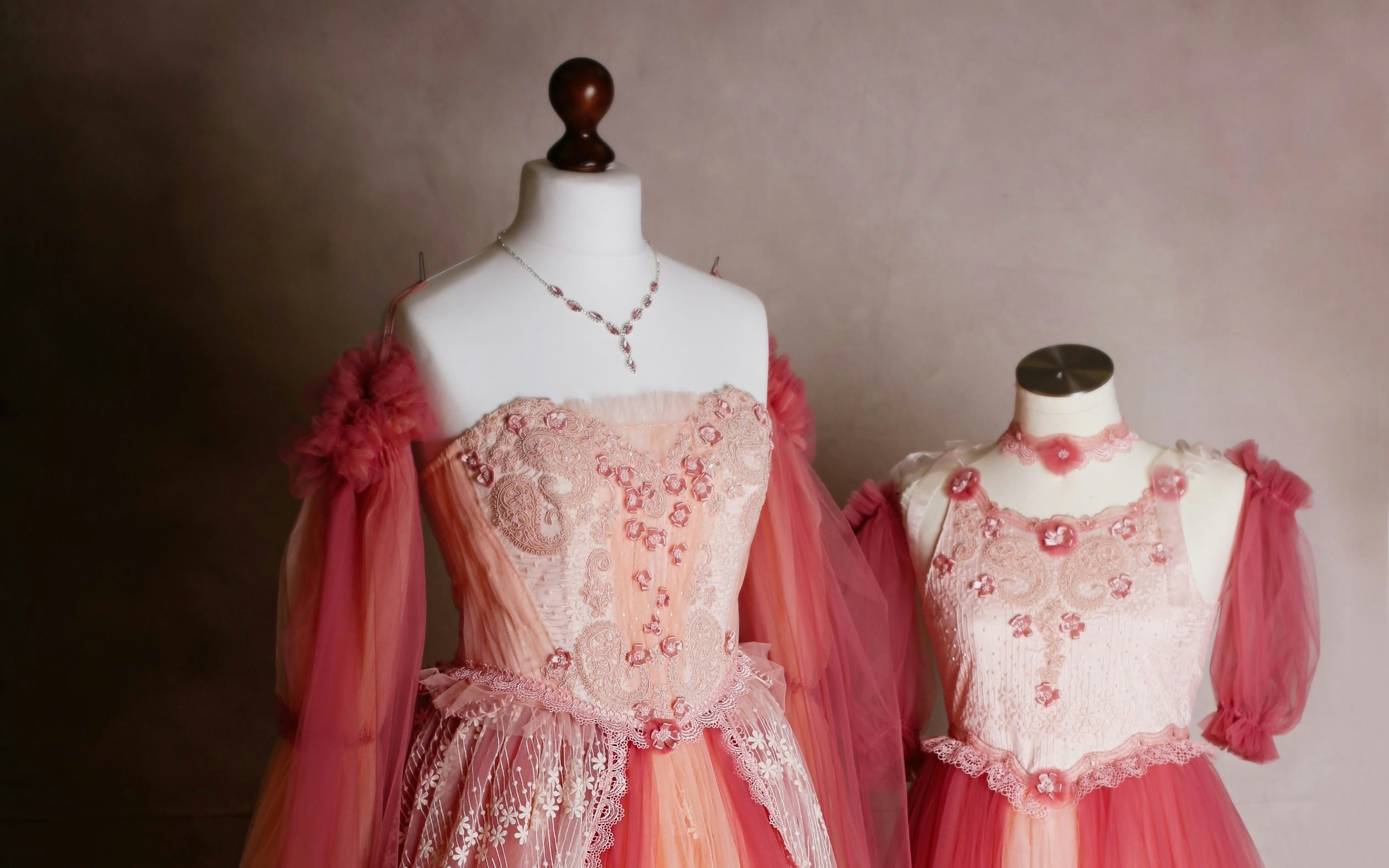 Pink gown costumes with floral lace details on mannequins.