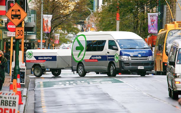 Super Shuttle van on city street for airport transfers.