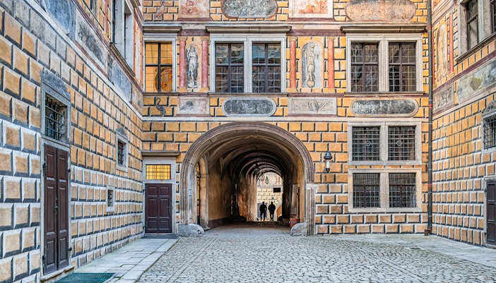 Intricate courtyard passage in Cesky Krumlov Castle with detailed frescoes and cobblestone path.