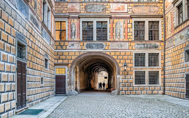 Intricate courtyard passage in Cesky Krumlov Castle with detailed frescoes and cobblestone path.