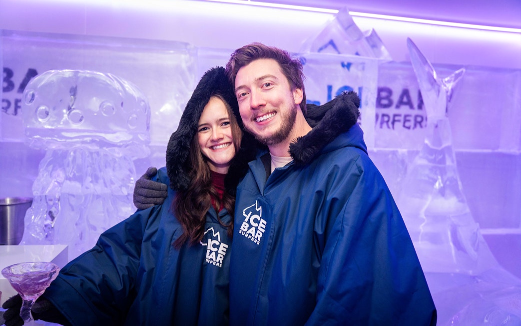 Couple in blue parkas enjoying IceBar Surfers Paradise with ice sculptures in the background.