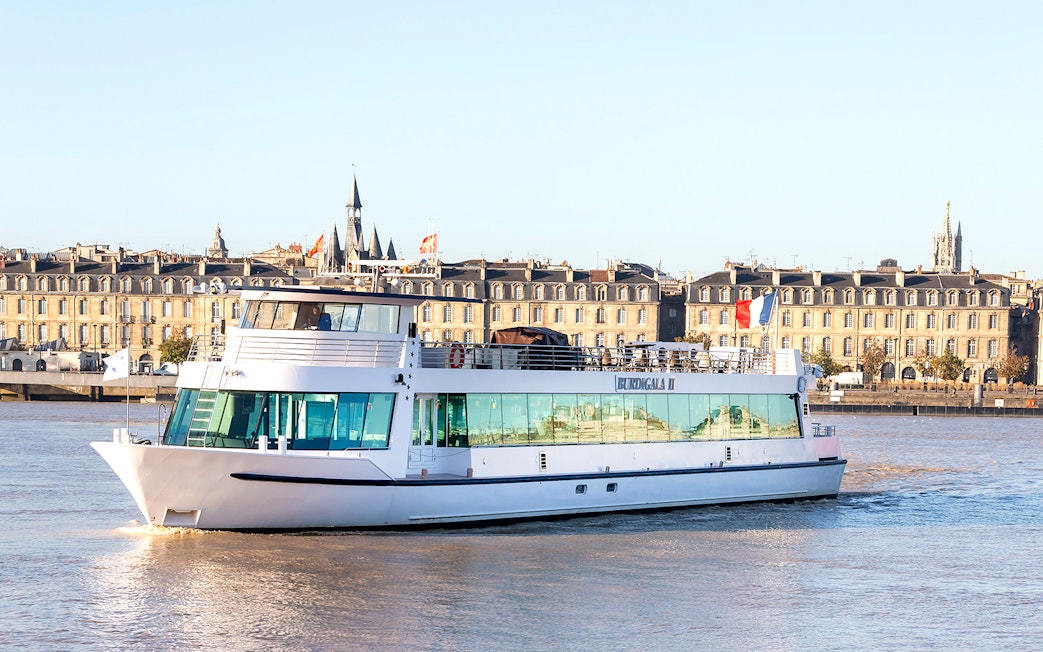 River cruise boat on the Garonne with Bordeaux cityscape in the background.