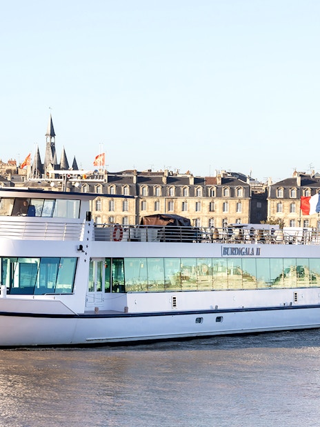 River cruise boat on the Garonne with Bordeaux cityscape in the background.