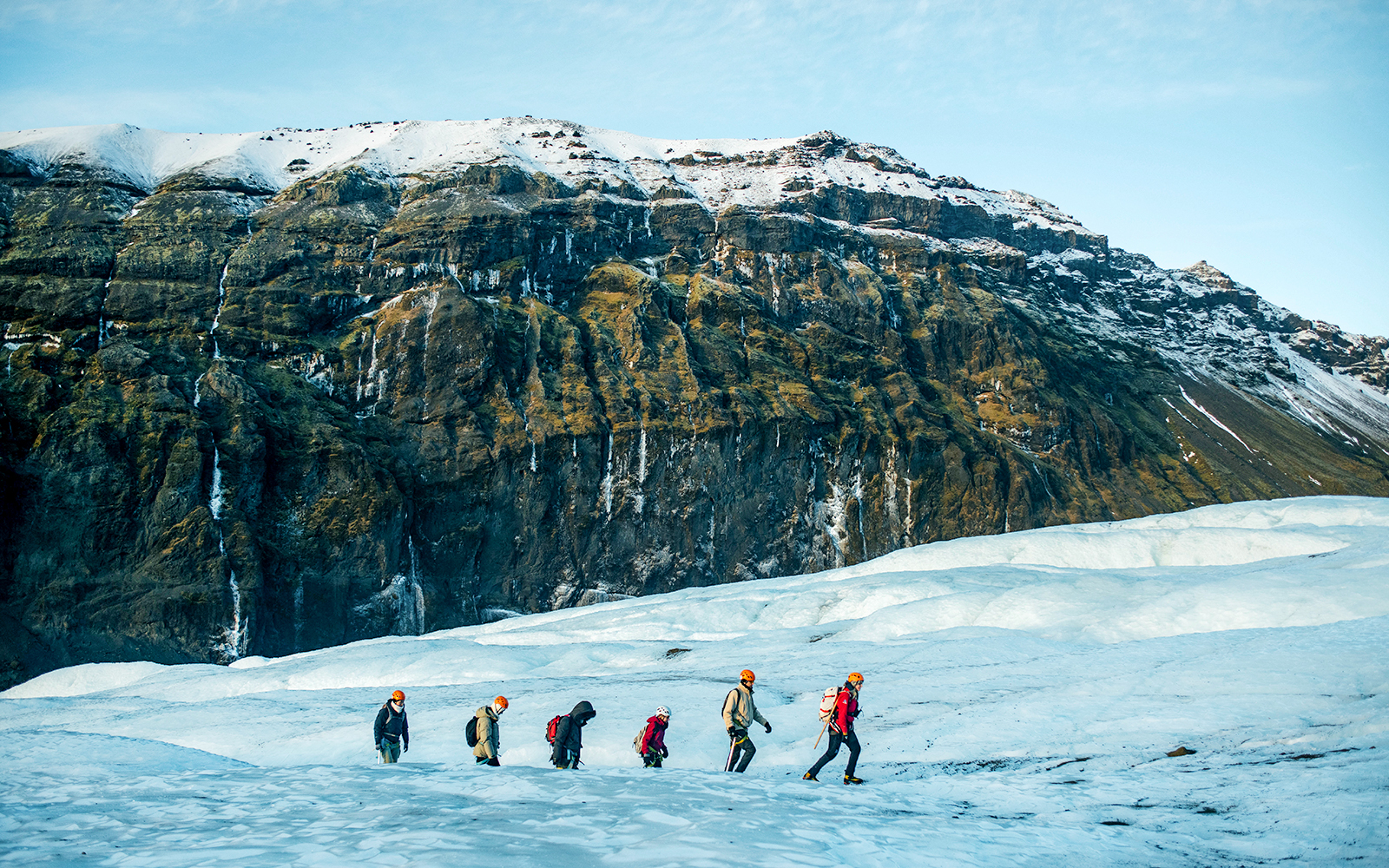 Hikers trekking on Vatnajökull Glacier in Iceland with snowy mountains in the background.