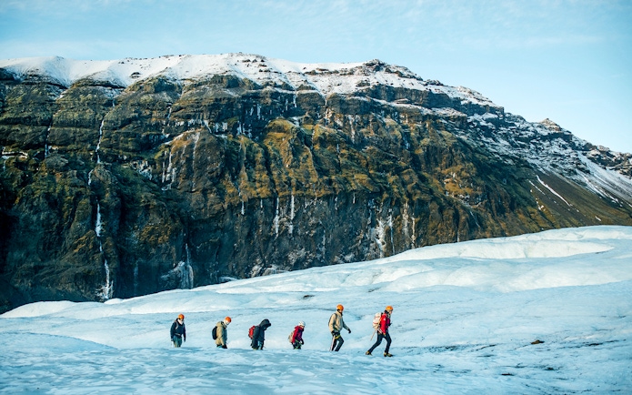 Hikers trekking on Vatnajökull Glacier in Iceland with snowy mountains in the background.