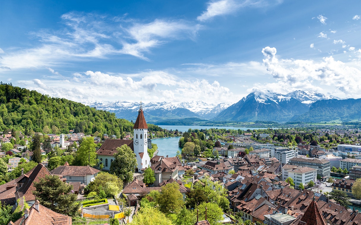 Aerial view of Thun with church tower, river, and Alps in the background.