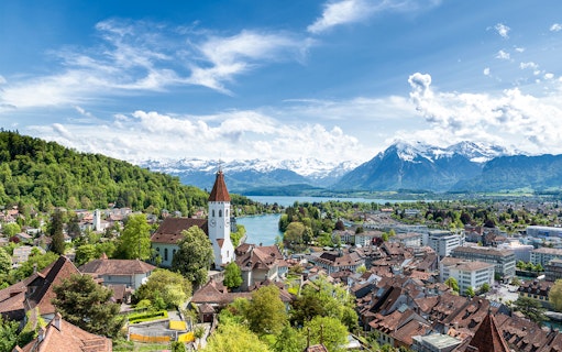 Aerial view of Thun with church tower, river, and Alps in the background.