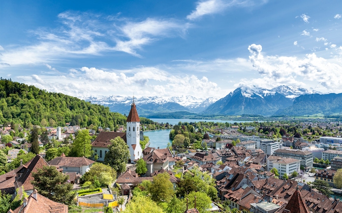 Aerial view of Thun with church tower, river, and Alps in the background.