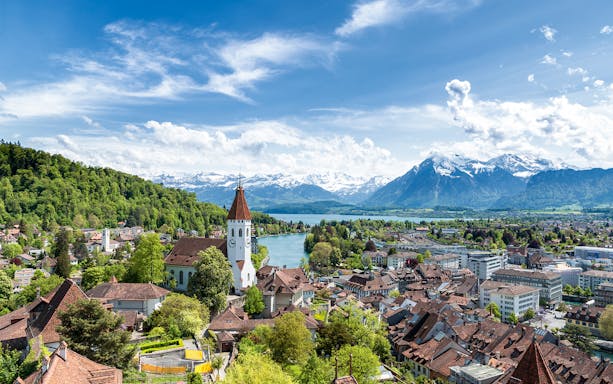Aerial view of Thun with church tower, river, and Alps in the background.