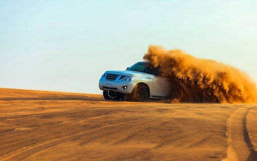 SUV driving through desert sand dunes in Dubai.