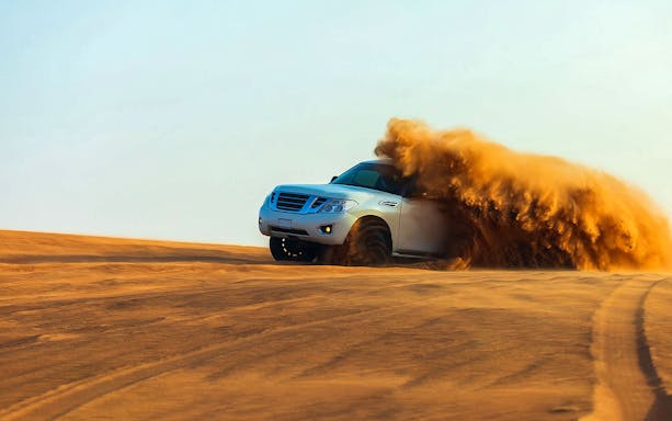 SUV driving through desert sand dunes in Dubai.