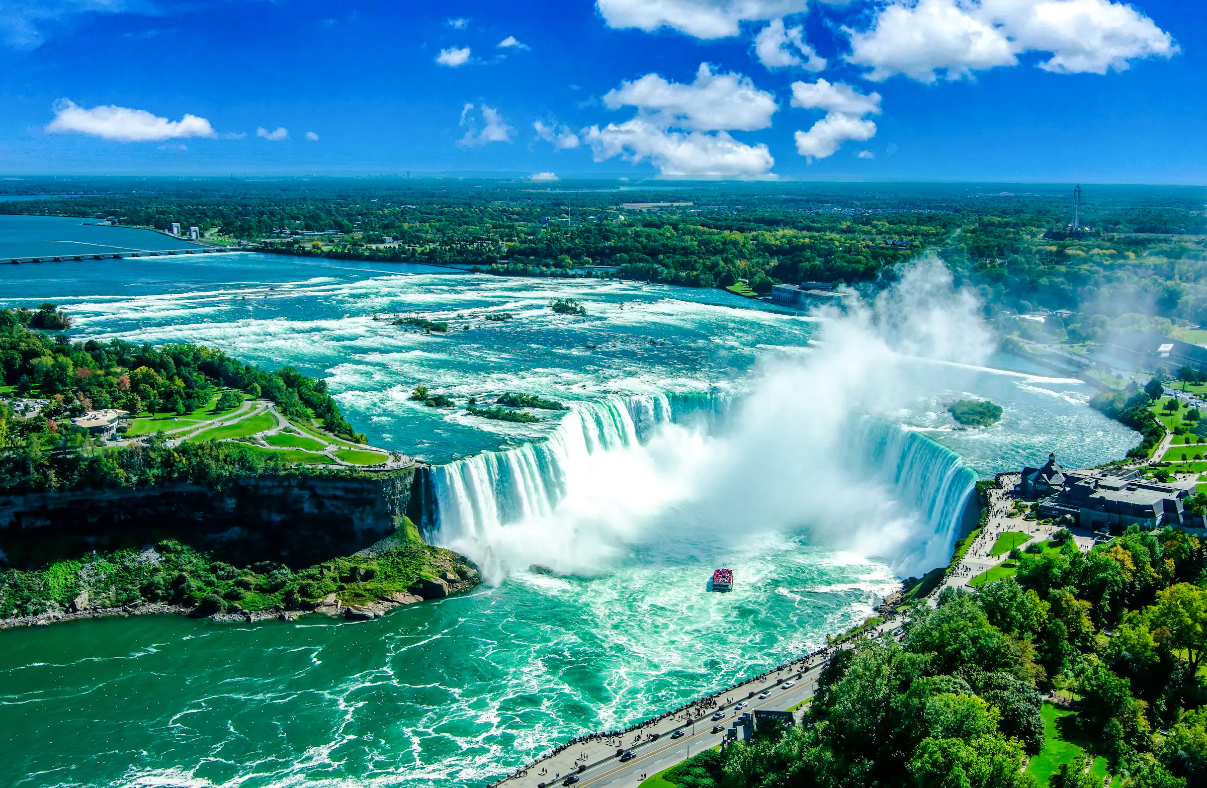 Niagara Falls aerial view with boat tour, lush greenery, and mist, part of Toronto small-group tour.