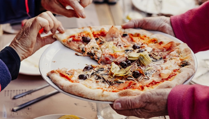Pizza with olives and artichokes being shared at Mediterráneo Pizzeria.