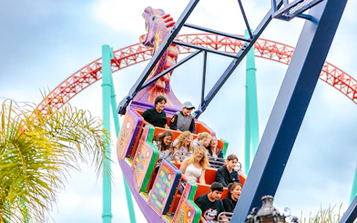 Riders enjoying the Dragon Swing at Knott's Berry Farm with roller coaster in background.