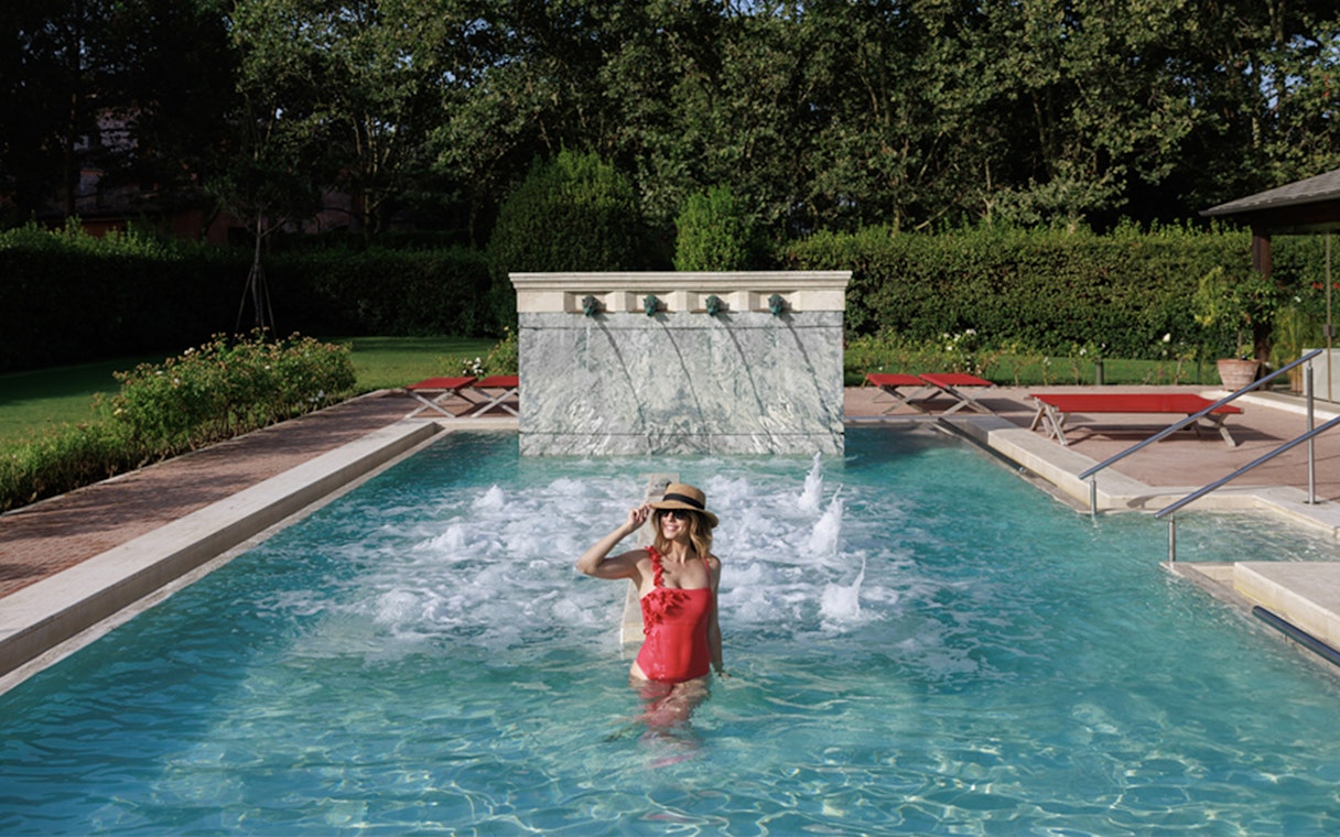 Person enjoying a pool at QC Terme Roma with water jets and greenery.