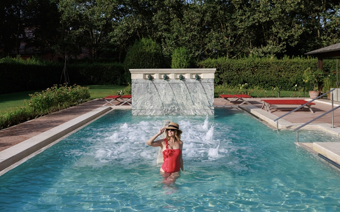 Person enjoying a pool at QC Terme Roma with water jets and greenery.