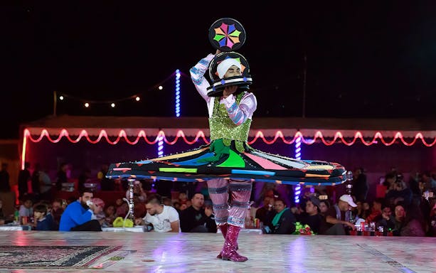 Performer in colorful attire spinning during evening desert safari show.