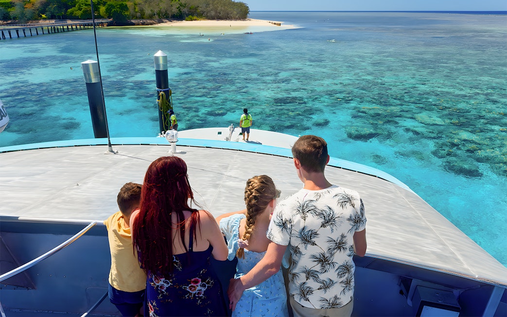 Tourists on a boat approaching Green Island, clear waters visible, Cairns half-day cruise.
