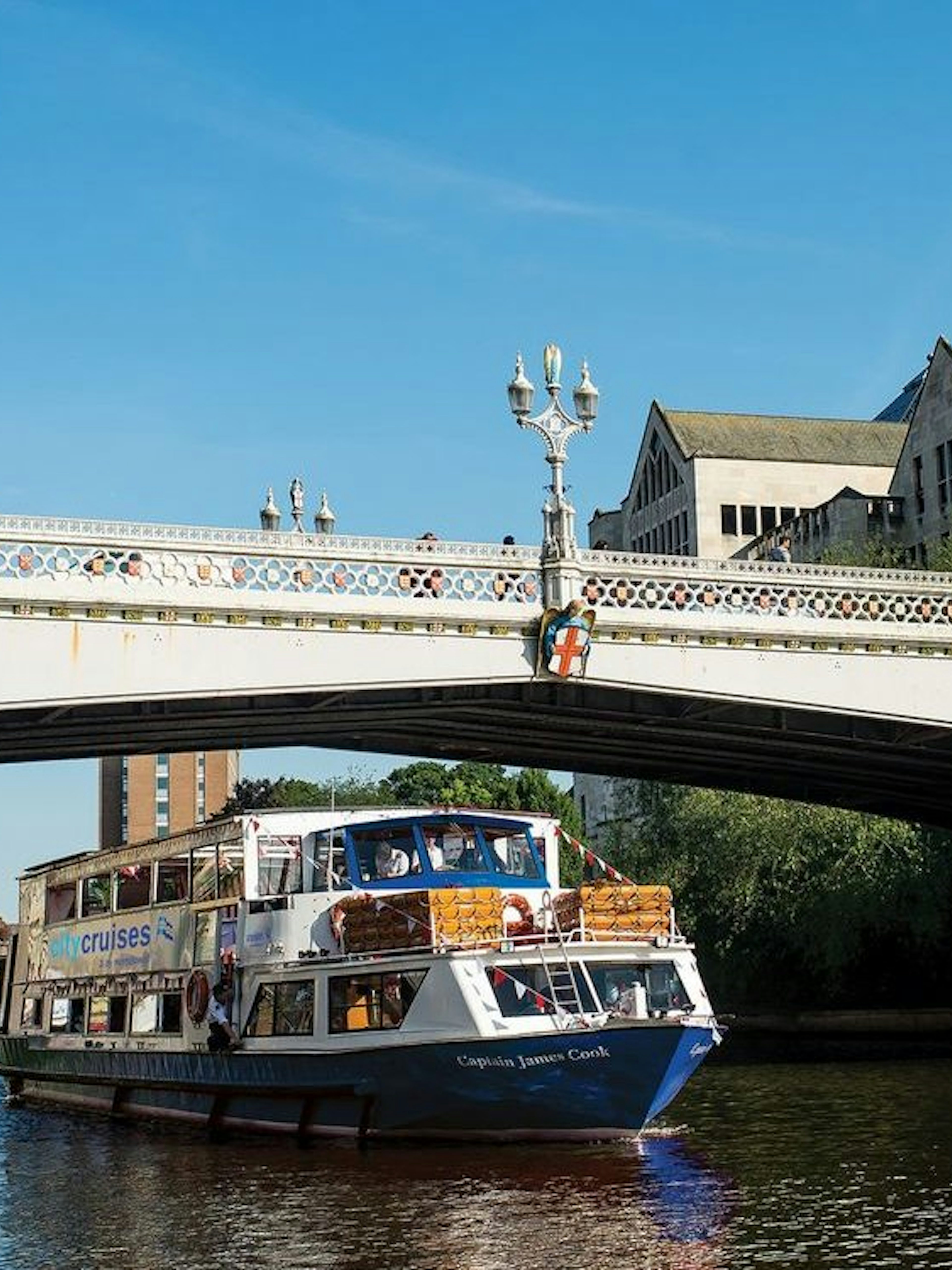 York sightseeing cruise boat passing under a historic bridge on a sunny day.