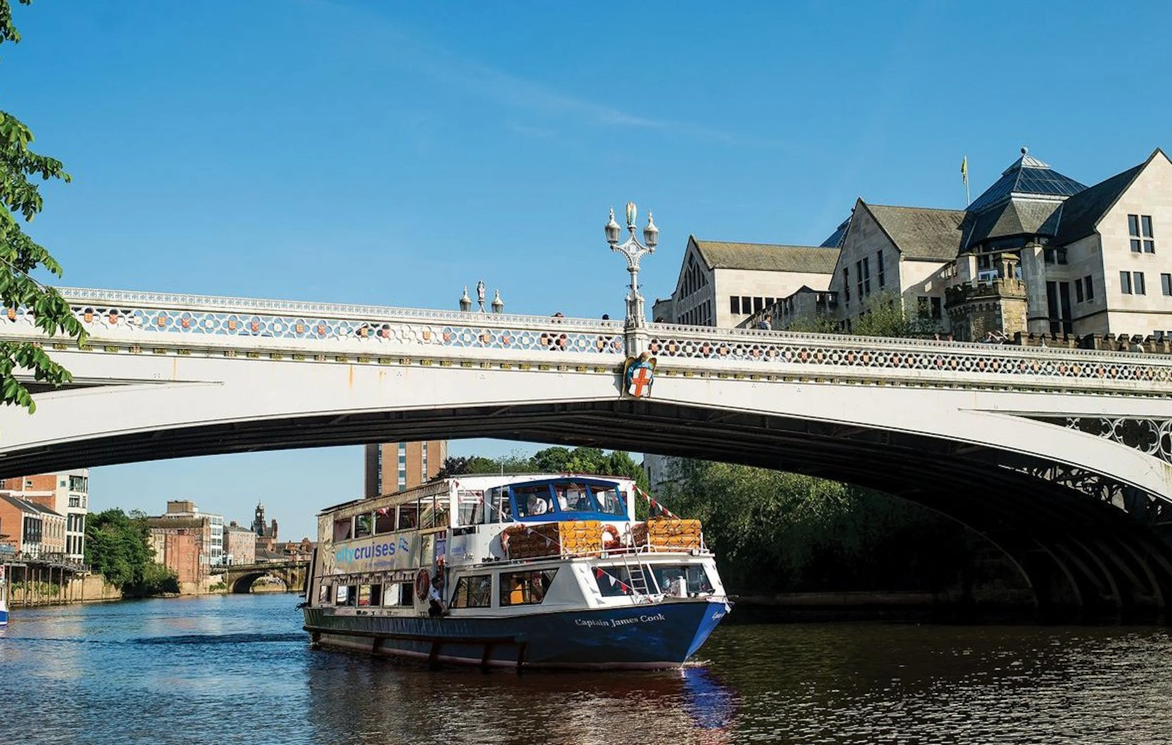 York sightseeing cruise boat passing under a historic bridge on a sunny day.