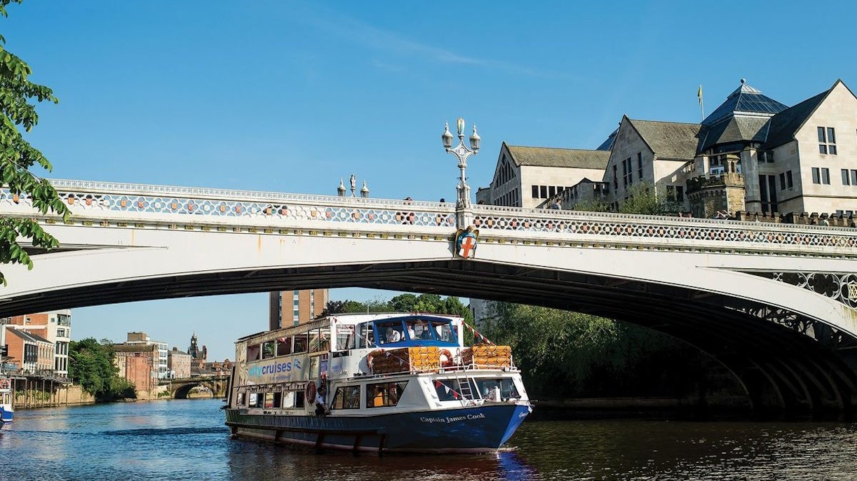 York sightseeing cruise boat passing under a historic bridge on a sunny day.