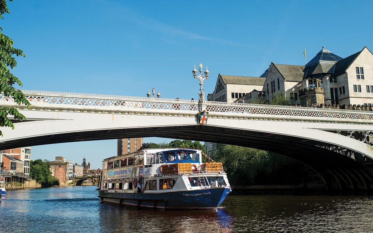 York sightseeing cruise boat passing under a historic bridge on a sunny day.