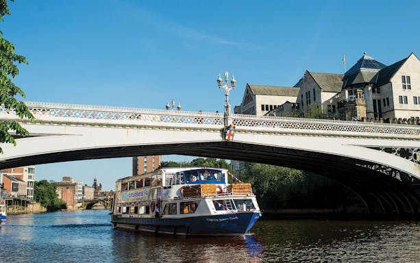 York sightseeing cruise boat passing under a historic bridge on a sunny day.
