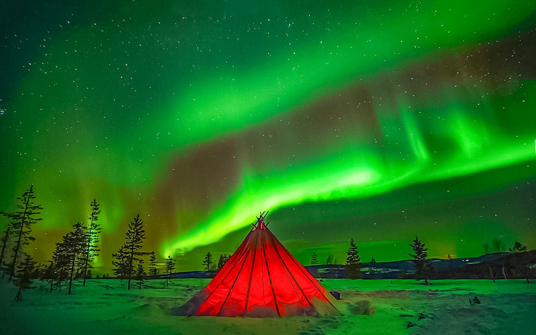 Northern Lights over a red tent in snowy Rovaniemi landscape.