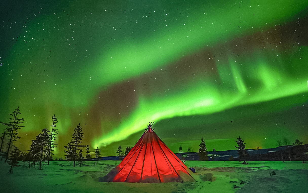 Northern Lights over a red tent in snowy Rovaniemi landscape.