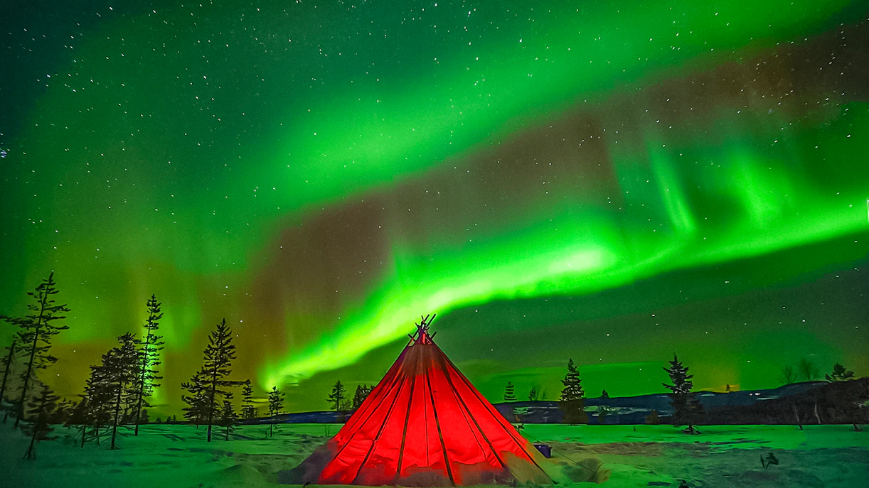 Northern Lights over a red tent in snowy Rovaniemi landscape.