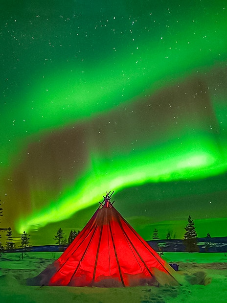 Northern Lights over a red tent in snowy Rovaniemi landscape.