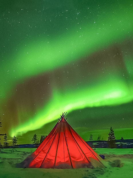 Northern Lights over a red tent in snowy Rovaniemi landscape.