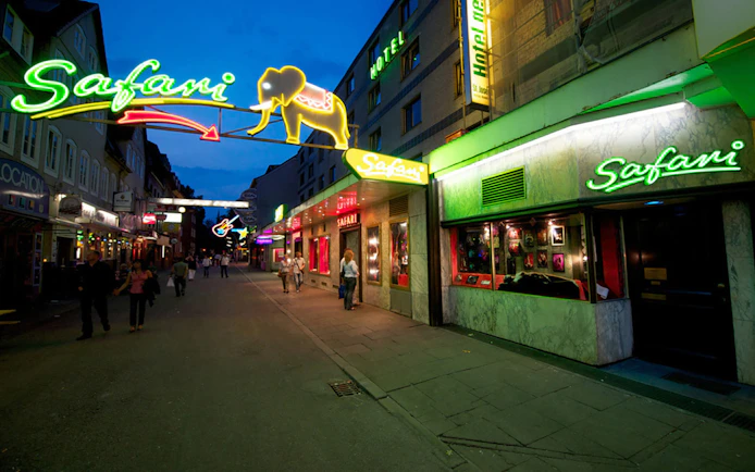Neon-lit street with Safari signs and people walking in a city nightlife area.