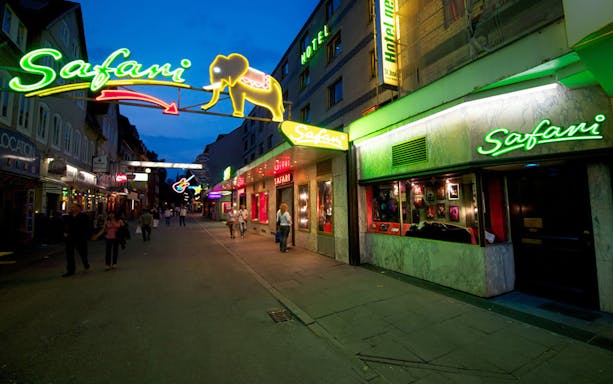 Neon-lit street with Safari signs and people walking in a city nightlife area.
