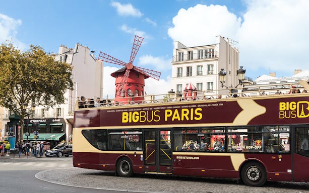Open-top tour bus in front of the Moulin Rouge in Paris.