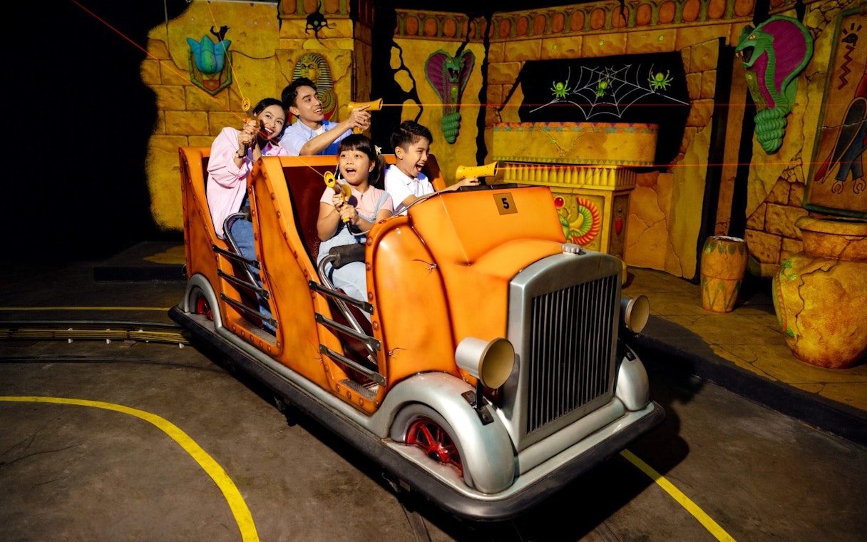 Family enjoying Laser Raiders ride at Legoland Malaysia, shooting targets in an ancient temple setting.