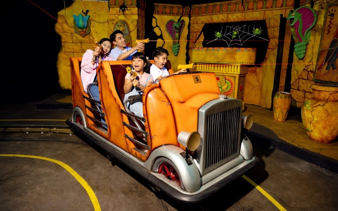 Family enjoying Laser Raiders ride at Legoland Malaysia, shooting targets in an ancient temple setting.