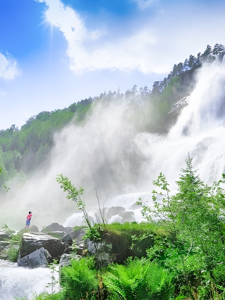 Tvindefossen waterfall with multiple streams cascading down a lush green cliff in Norway.
