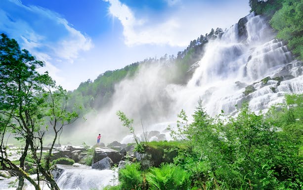Tvindefossen waterfall with multiple streams cascading down a lush green cliff in Norway.