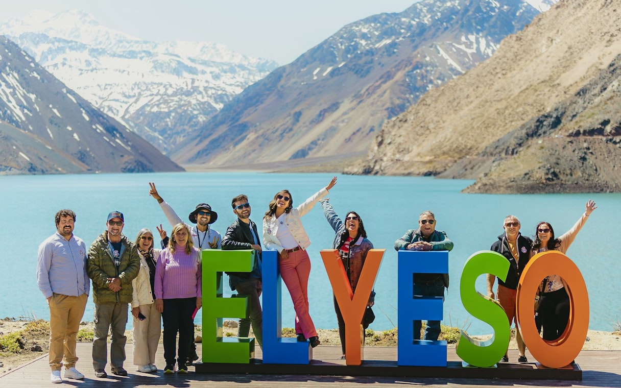 Group enjoying a tour at Embalse El Yeso, Chile, with mountains and lake in the background.